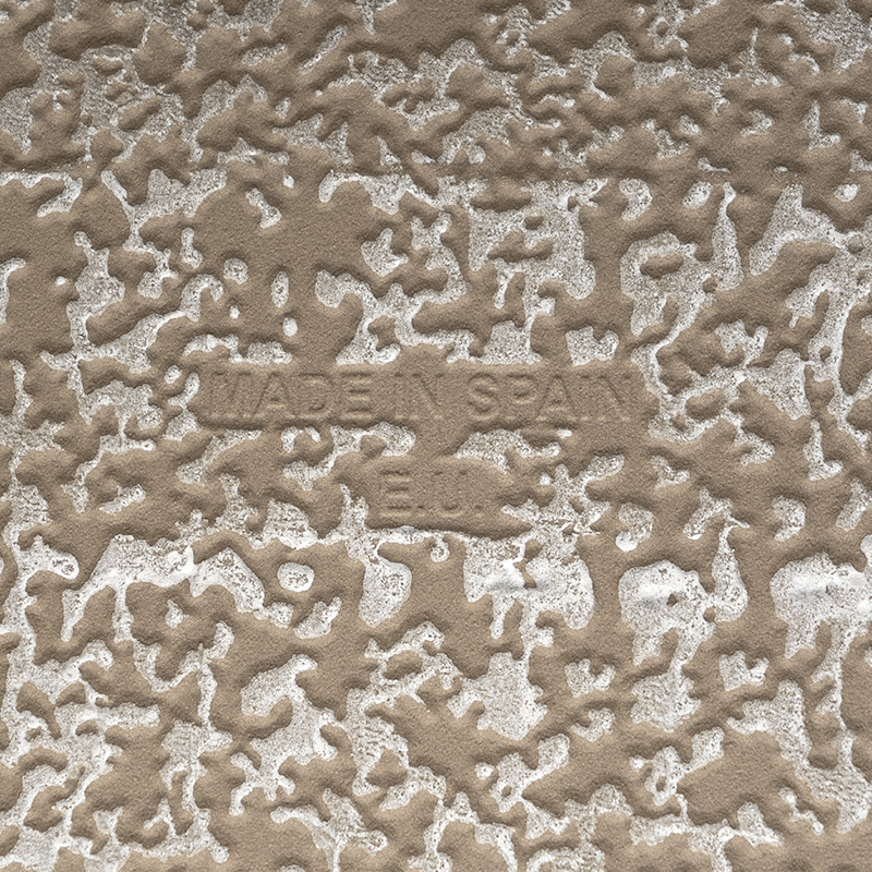 A textured tile features embossed text reading `MADE IN SPAIN` against a speckled gray and beige background. The surface appears