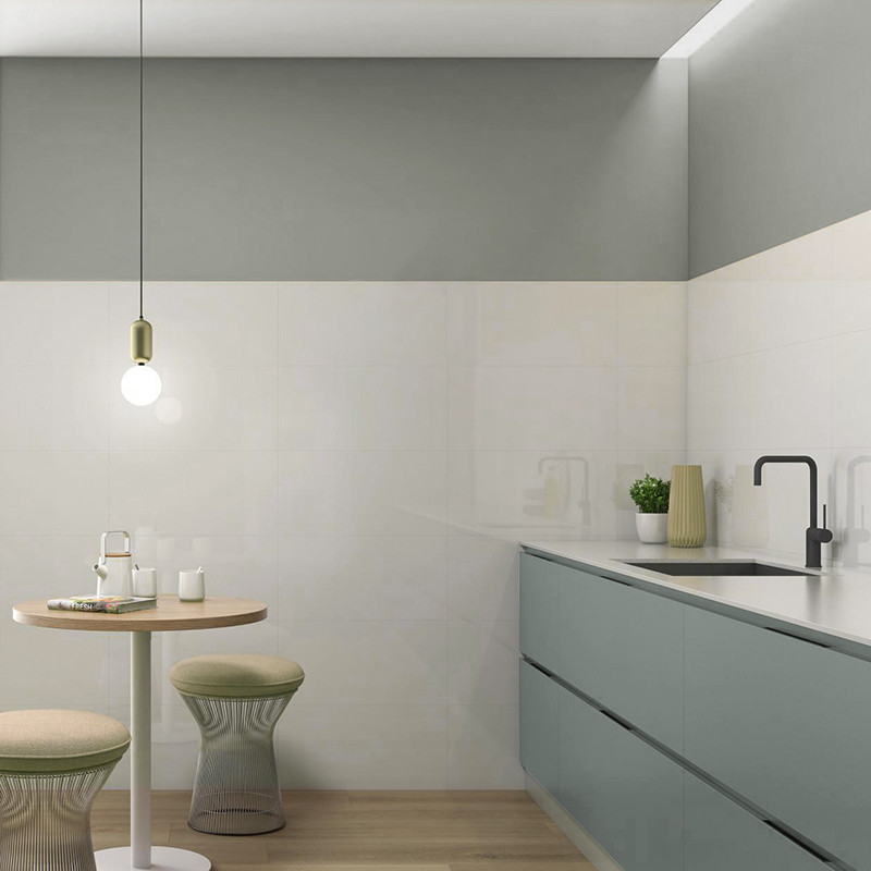A modern kitchen features sleek, matte sage-green cabinets along a wall. A round table with two stools sits beneath a hanging bu