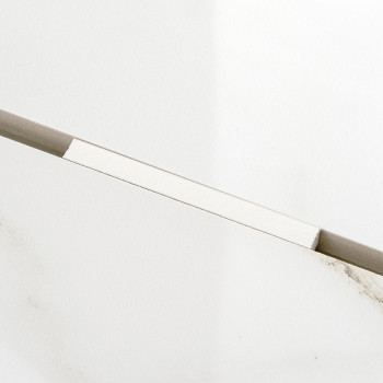 Een rechthoekige, lichtgekleurde tegel rust diagonaal tegen een effen witte achtergrond en vertoont subtiele grijze nerven en ee