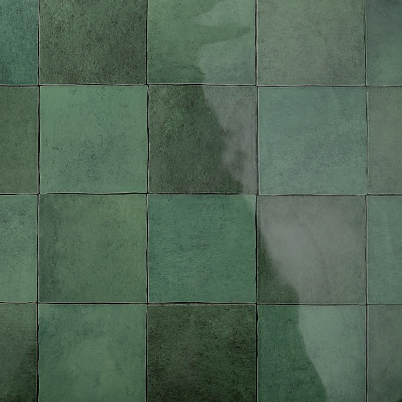 Les carreaux carrés verts disposés en grille réfléchissent la lumière, créant une surface brillante. Ils forment un motif contin