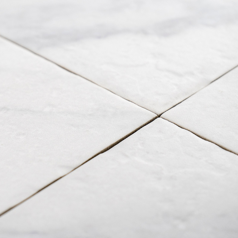 Quatro ladrilhos quadrados brancos se encontram nos cantos, formando um padrão em `X`, com leve textura visível, sugerindo uma s