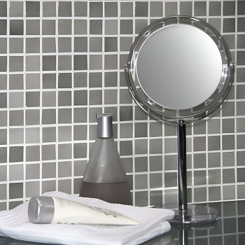 Der Spiegel steht neben einer Pumpflasche und einer Cremetube auf Handtüchern und spiegelt sich vor einer Glasmosaikwand mit Git