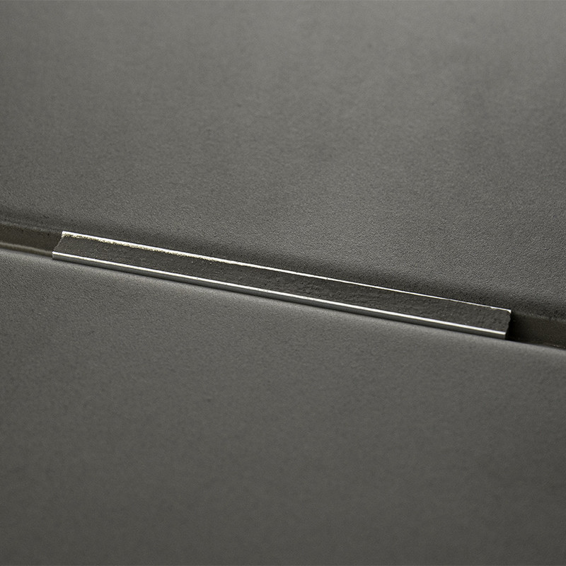 Un carreau gris foncé avec une barre métallique incrustée sur sa surface, réfléchissant la lumière, sur un fond lisse et minimal