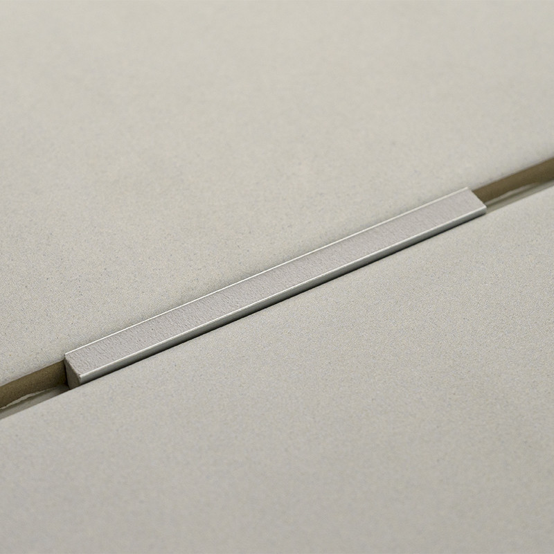 Een gladde, rechthoekige metalen handgreep rust over twee aangrenzende, licht getextureerde crèmekleurige tegels, waardoor een m