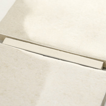 Eine beige, rechteckige Fliese liegt auf einem Stapel ähnlicher Fliesen und ergibt ein ordentliches, geordnetes Muster in einer 