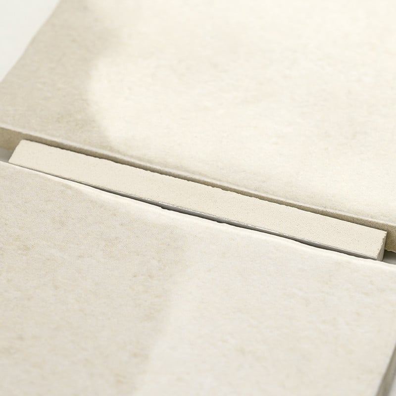 Un carreau rectangulaire beige repose sur une pile de carreaux similaires, créant un motif soigné et ordonné dans un cadre neutr