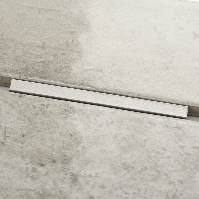 Un carreau rectangulaire affiche une texture marbrée lisse et subtile dans des tons de gris. Il est adjacent à une étroite bande