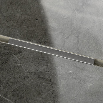 Eine rechteckige graue Fliese, diagonal halbiert, zeigt eine Naht mit unterschiedlichen Grautönen. Die Oberfläche weist eine dez