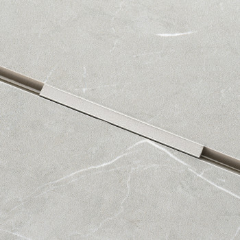 A rectangular, light grey tile features a subtle marble pattern with faint white veins. A thin, horizontal metallic strip inters