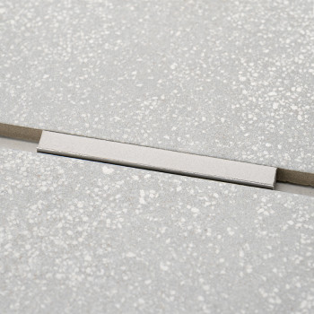 Ein rechteckiger, silberner Einsatz durchbricht das einheitliche Muster der hellgrauen, gesprenkelten Fliesen und bildet einen s