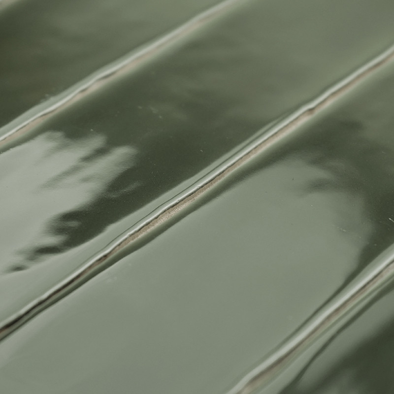 Carreau de céramique vert brillant présentant un motif nervuré en relief aux reflets subtils. Le carreau est posé à plat, présen