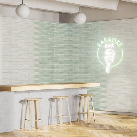 Eine minimalistische Bar-Atmosphäre mit drei Holzhockern an einer Betontheke. Ein Neonschild mit der Aufschrift „KARAOKE BAR“ un