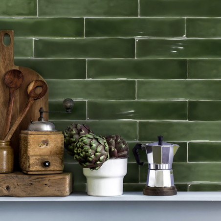 Grüne rechteckige Fliesen säumen eine Küchenwand. Auf einem Regal stehen Holzutensilien, eine Vintage-Mühle, Artischocken in ein
