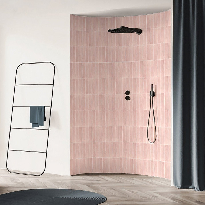 Gebogen muur met roze tegels met een zwarte douchekop en bedieningselementen, omgeven door een moderne badkamer met handdoekenre