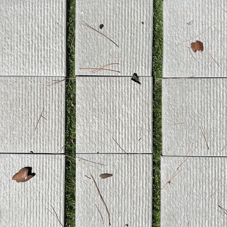 Rectangular beige tiles rest on grass, scattered with dry leaves and pine needles, creating a natural, textural contrast. Rectangular beige tiles rest on grass, scattered with dry leaves and pine needles, creating a natural, textural contrast.