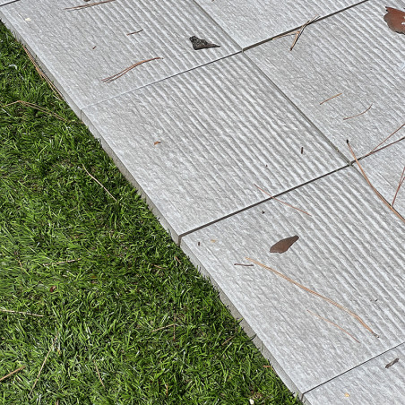 Gray, ribbed tiles lie flat, scattered with dry leaves and twigs. The tiles border a patch of lush, green grass. Gray, ribbed tiles lie flat, scattered with dry leaves and twigs. The tiles border a patch of lush, green grass.