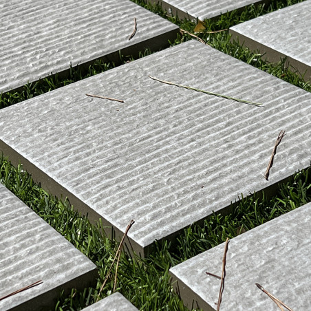 Square stone tiles lie evenly spaced on lush green grass, featuring textured ridges with scattered slender twigs resting on thei Square stone tiles lie evenly spaced on lush green grass, featuring textured ridges with scattered slender twigs resting on thei