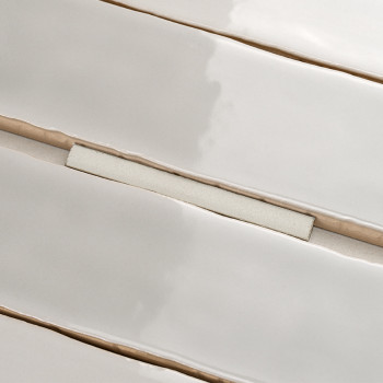 Rechteckige Keramikfliesen, leicht uneben und glänzend, liegen in parallelen Reihen. Sie sind durch beige Fugenlinien getrennt, 