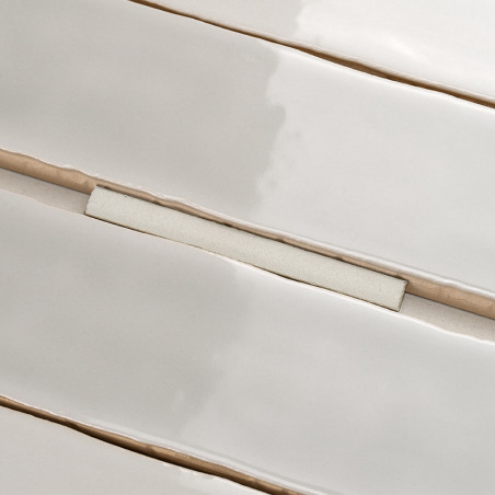 Rechteckige Keramikfliesen, leicht uneben und glänzend, liegen in parallelen Reihen. Sie sind durch beige Fugenlinien getrennt,  Rechteckige Keramikfliesen, leicht uneben und glänzend, liegen in parallelen Reihen. Sie sind durch beige Fugenlinien getrennt,