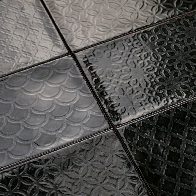 Los azulejos negros brillantes presentan varios patrones en relieve, que incluyen escamas, motivos florales y diseños geométrico