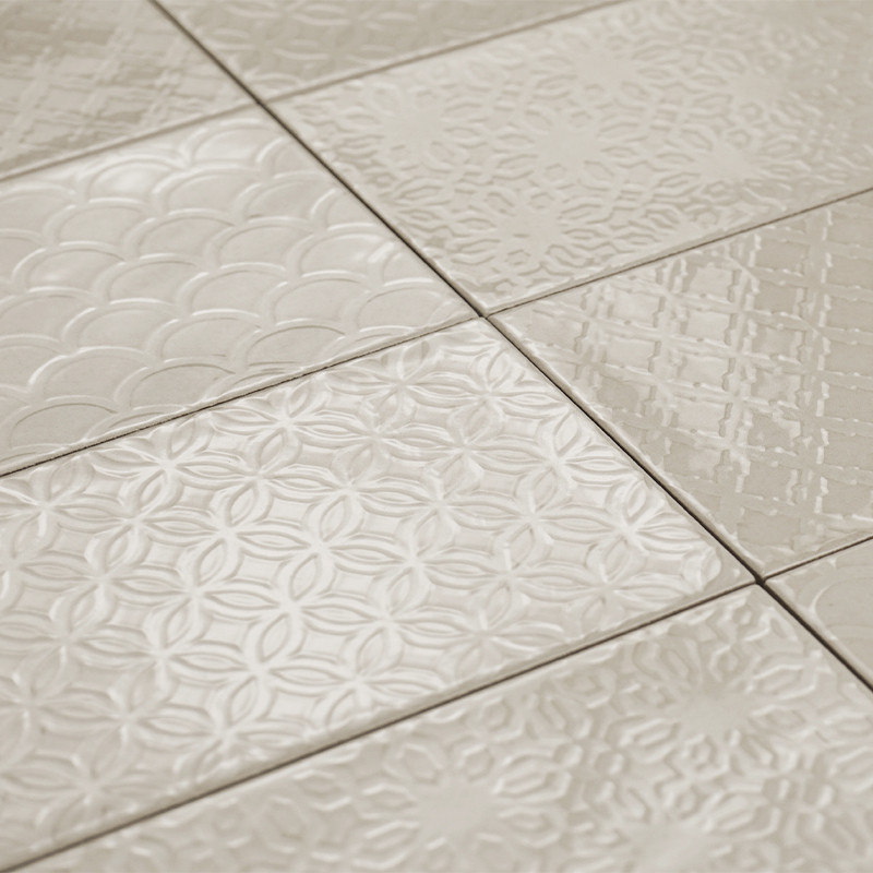 Les carreaux de céramique présentent divers motifs géométriques en relief, créant une surface texturée dans un ton beige neutre,
