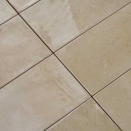 Crèmekleurige keramische tegels vormen een raster en reflecteren het licht zachtjes over hun glanzende oppervlakken. De voegenli