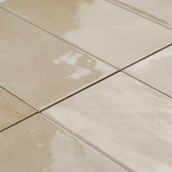 Rectangular ceramic tiles, laid in a grid pattern, exhibit an alternating mix of matte and glossy beige surfaces, suggesting a c