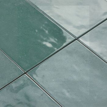 Grüne Keramikfliesen erscheinen unter Licht glänzend und sind in einem Gittermuster verlegt. Ihre reflektierende Oberfläche verl