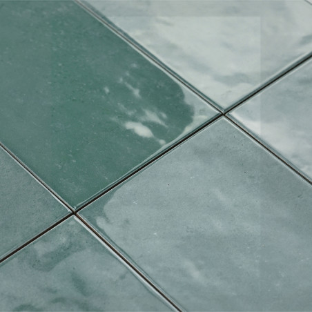 Grüne Keramikfliesen erscheinen unter Licht glänzend und sind in einem Gittermuster verlegt. Ihre reflektierende Oberfläche verl