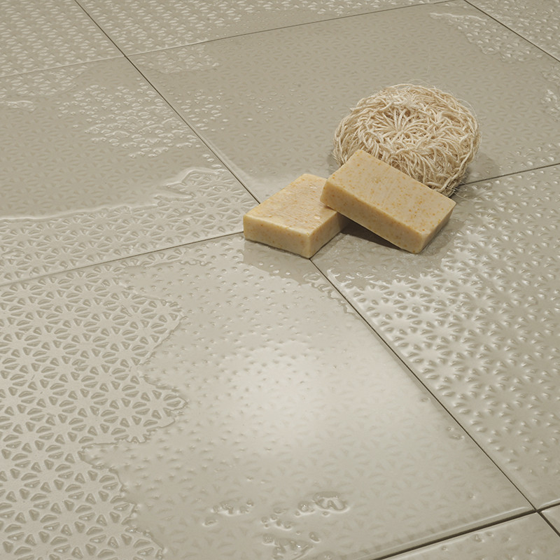 Glossy beige tiles with intricate embossed patterns are set against each other, holding a loofah and two soap bars on their smoo