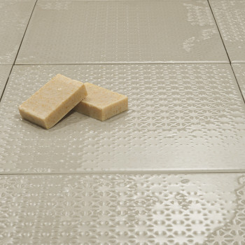 Neutral strukturierte Fliesen liegen flach und reflektieren das Licht subtil. Darauf ruhen zwei rechteckige Seifen, die für eine