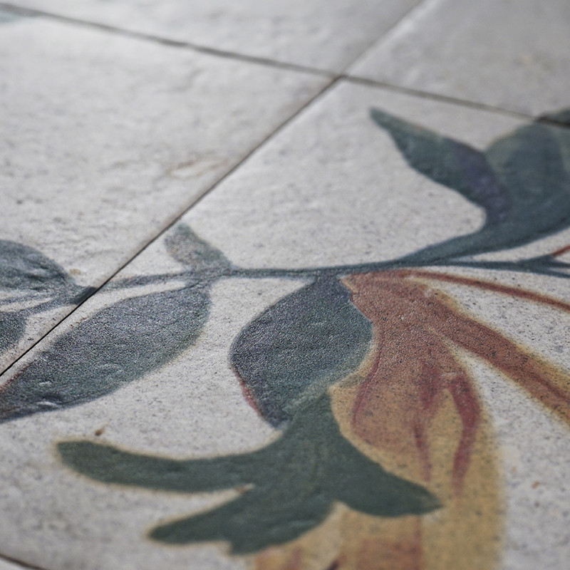 Um azulejo com desenho floral exibe folhas verdes e marrons, sugerindo uma decoração artística. O motivo se espalha por uma supe