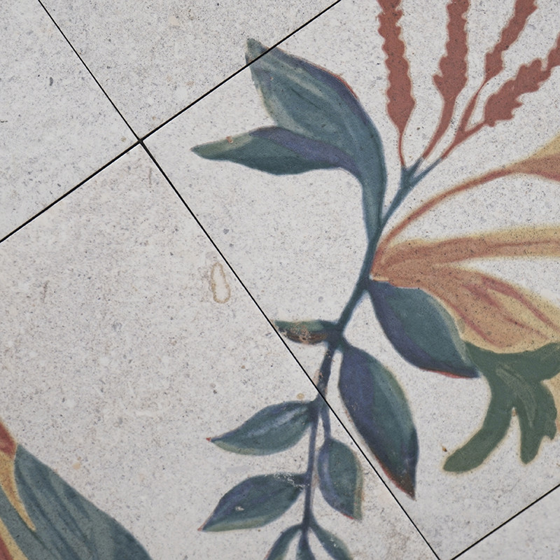 Los azulejos de cerámica presentan un diseño floral con hojas verdes y flores rojas. El patrón se extiende a lo largo de cuatro 