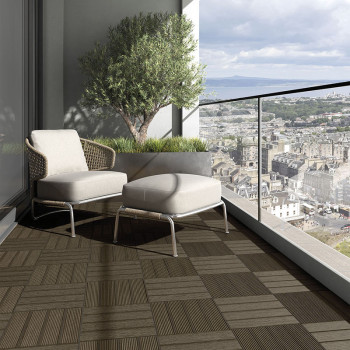 Une chaise et un pouf en osier reposent sur un balcon à motifs géométriques, surplombant un vaste paysage urbain avec des montag