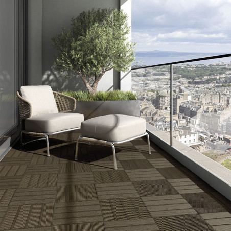Une chaise et un pouf en osier reposent sur un balcon à motifs géométriques, surplombant un vaste paysage urbain avec des montag