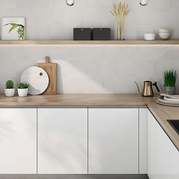 Weiße Küchenschränke stehen unter einer Arbeitsplatte aus hellem Holz, dekoriert mit Topfpflanzen und Utensilien, darunter ein H