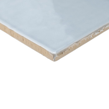 A glossy, light blue ceramic tile with a smooth surface rests at an angle, showcasing its unfinished beige edge against a white 