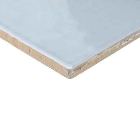 Eine glänzende, hellblaue Keramikfliese mit glatter Oberfläche liegt schräg und zeigt ihre unbearbeitete beige Kante vor einem w Eine glänzende, hellblaue Keramikfliese mit glatter Oberfläche liegt schräg und zeigt ihre unbearbeitete beige Kante vor einem w