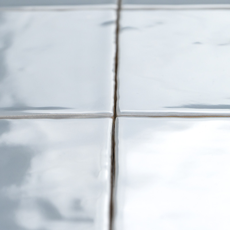 Four glossy, white ceramic tiles fit together, their surfaces reflecting light. Visible grout lines separate them, forming a sim