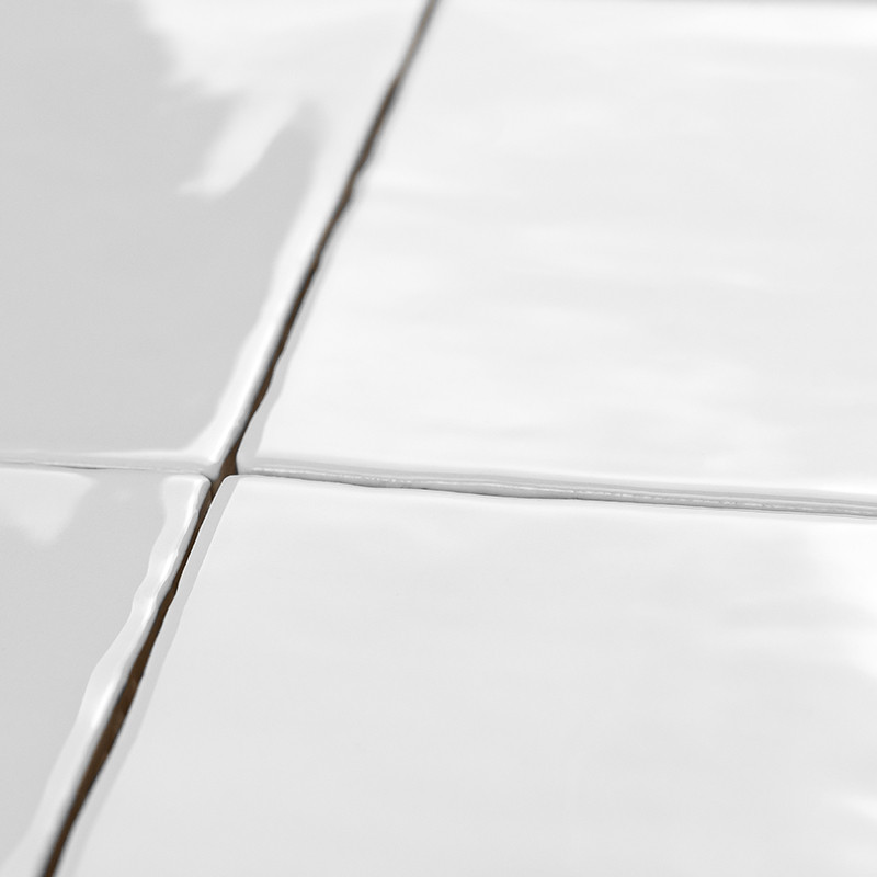 Les carreaux de céramique blanche s'alignent parfaitement avec les lignes de coulis visibles, réfléchissant la lumière, créant u