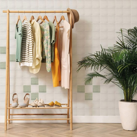 Auf einem Kleiderständer aus Holz hängen sechs Kleidungsstücke mit Hüten und Schuhen darunter. Es steht an einer gefliesten Wand