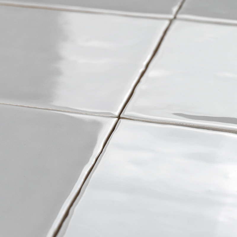 Witte keramische tegels vormen een raster met zichtbare voeglijnen, liggen plat en creëren een strak, reflecterend oppervlak in 