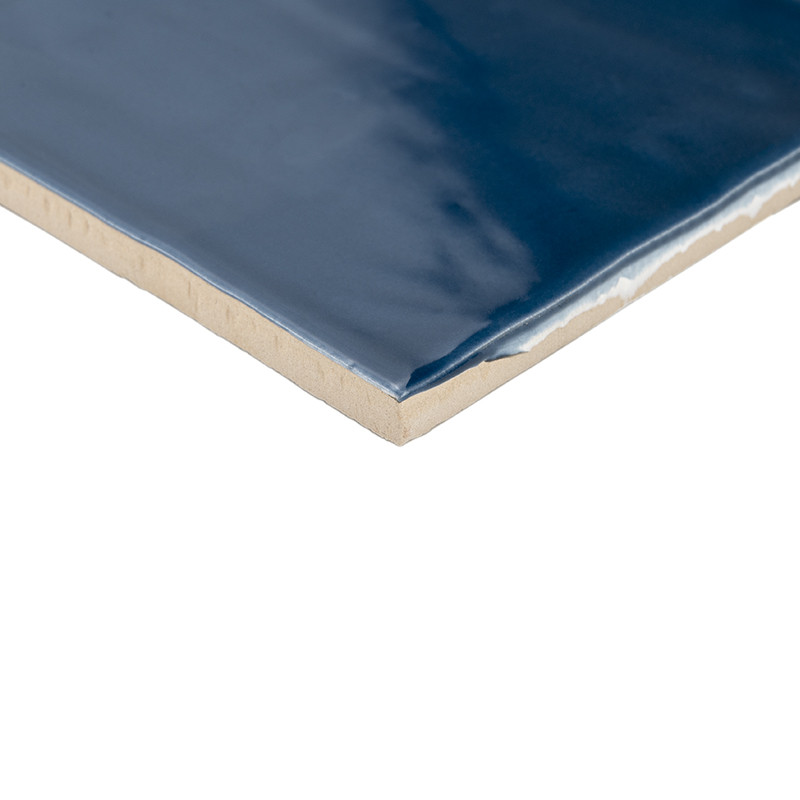 Un carreau de céramique rectangulaire présente une surface brillante d’un bleu profond. Ses bords dévoilent une sous-couche beig