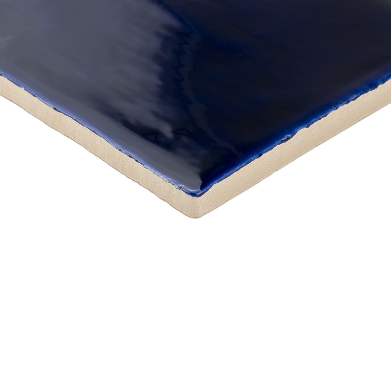 Um azulejo cerâmico brilhante e azul profundo reflete a luz, exibindo sua superfície lisa e vidrada contra uma borda bege e não 