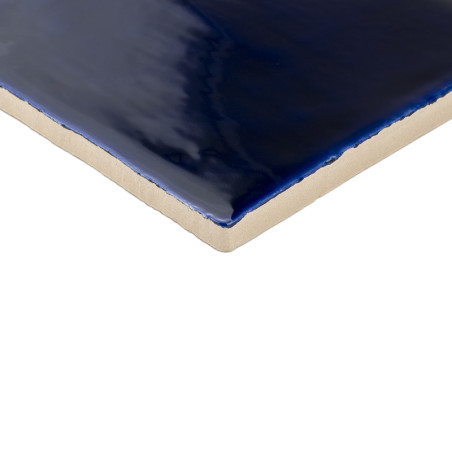 Eine glänzende, tiefblaue Keramikfliese reflektiert Licht und präsentiert ihre glatte, glasierte Oberfläche vor einem beigen, un Eine glänzende, tiefblaue Keramikfliese reflektiert Licht und präsentiert ihre glatte, glasierte Oberfläche vor einem beigen, un