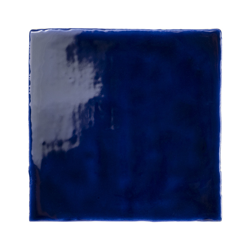 A glossy, square, deep blue tile reflects light, highlighting its smooth texture and monochromatic finish, set against a plain w