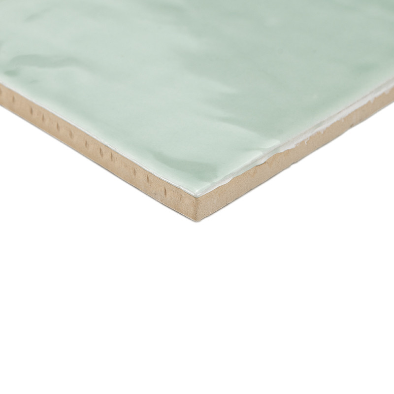 Un azulejo cerámico cuadrada con una superficie brillante de color verde claro descansa sobre un fondo blanco liso, mostrando su