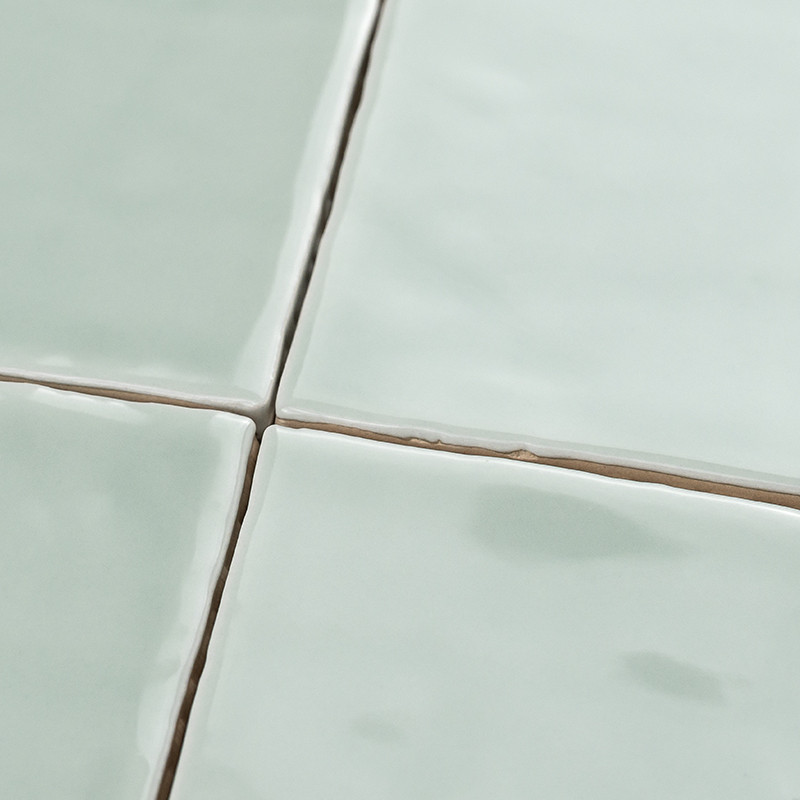 Four glossy, pale green ceramic tiles intersect, forming an uneven grid with visible grout lines in between them, creating a sim