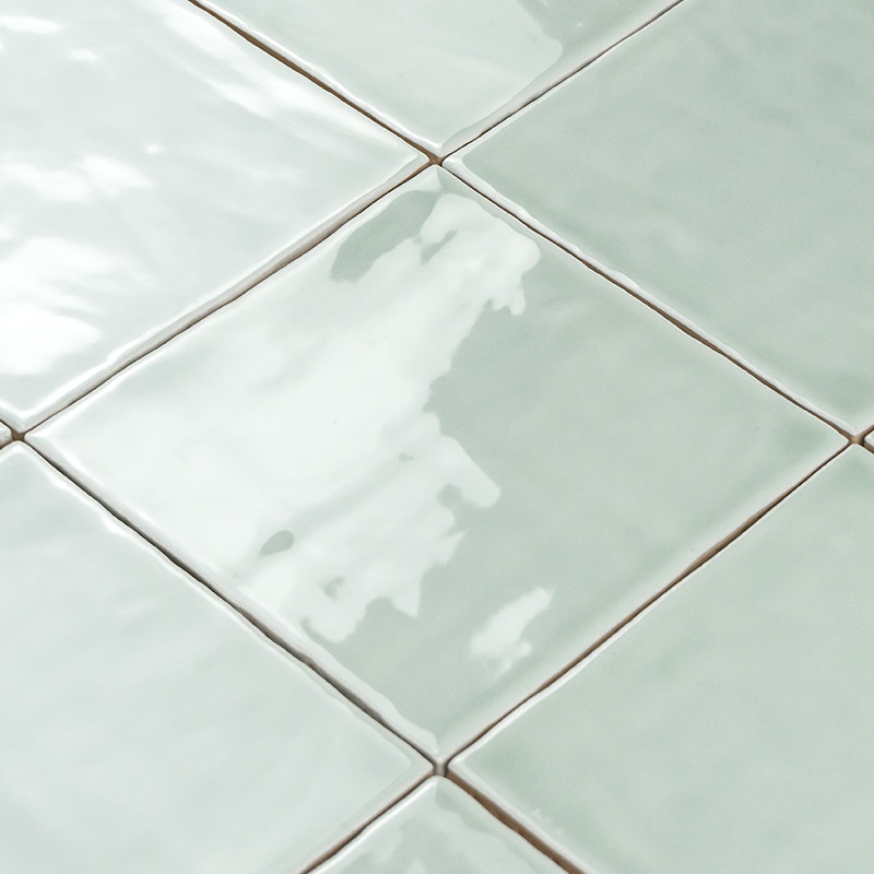 Vierkante keramische tegels die licht reflecteren, diagonaal gerangschikt in een rasterpatroon en een lichtgroene kleur vertonen