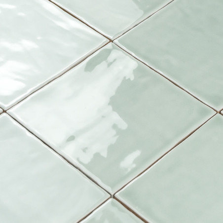 Ladrilhos cerâmicos quadrados refletindo a luz, dispostos diagonalmente em um padrão de grade, exibindo uma cor verde pálida em 